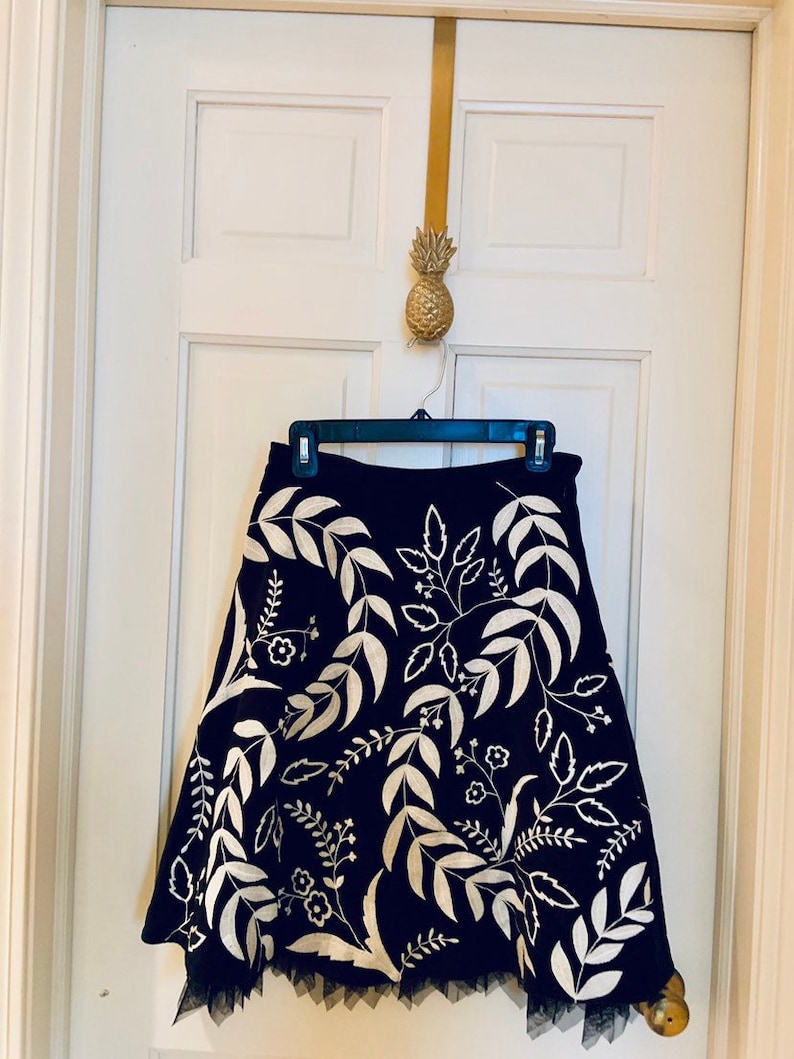 May include: A black skirt with a white floral embroidery design. The skirt has a tulle trim at the hem.