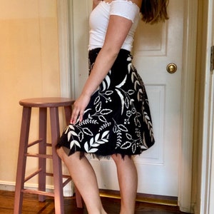 May include: A black skirt with a white floral pattern and a black tulle trim. The skirt is knee-length and has a fitted waist.