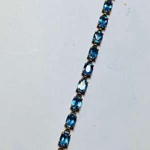 May include: A gold-toned bracelet featuring a series of oval, light blue gemstones. The gemstones are set in individual gold links, creating a delicate and elegant design. The bracelet is secured with a clasp.