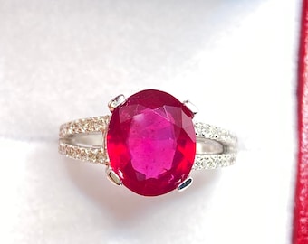 May include: A silver ring featuring a large oval ruby gemstone, surrounded by smaller diamonds. The ring has a split shank design.