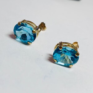 May include: A pair of gold earrings with oval-shaped blue topaz gemstones.