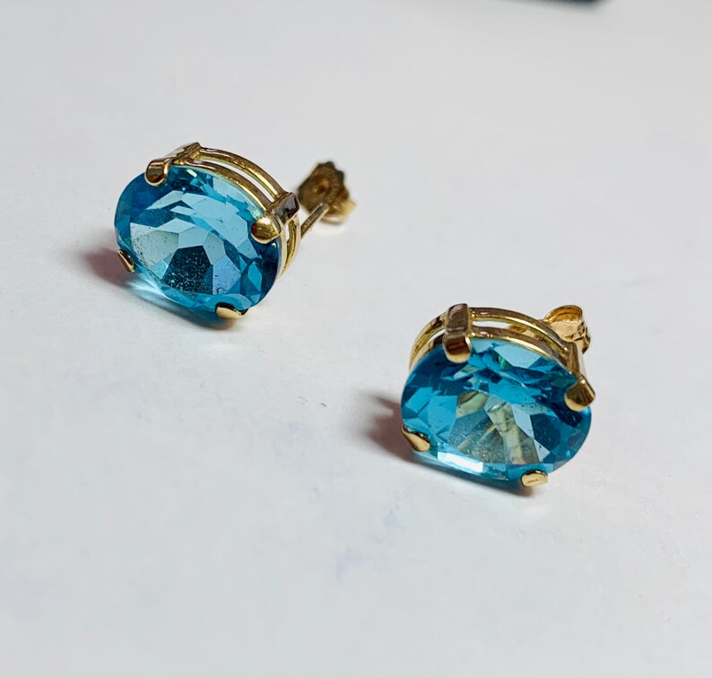 May include: A pair of gold earrings with oval-shaped blue topaz gemstones.