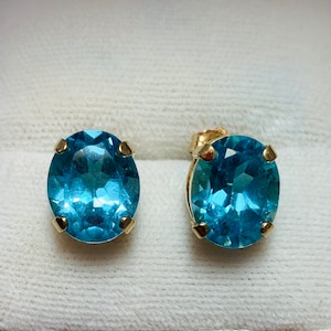 May include: A pair of gold earrings with oval-shaped blue topaz gemstones.