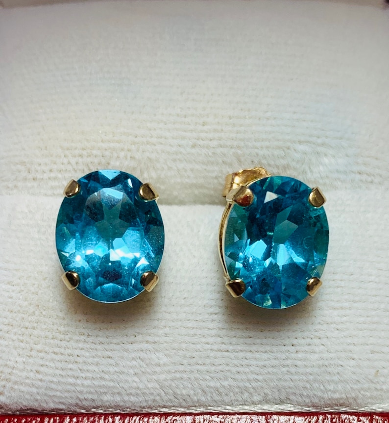 May include: A pair of gold earrings with oval-shaped blue topaz gemstones.