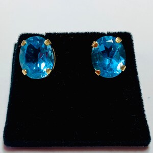 May include: A pair of oval-shaped blue topaz earrings with gold settings. The earrings are displayed on a black velvet background.