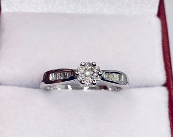 Könnte beinhalten: Ein silberner Ring mit einem Cluster aus kleinen Diamanten in der Mitte und kleineren Diamanten, die in die Band eingefasst sind.