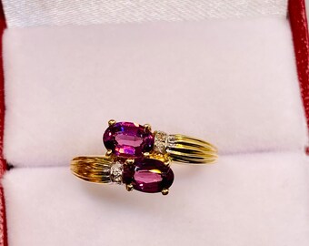 May include: A gold ring with two oval-shaped purple gemstones and small diamonds set in the band.