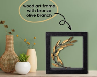 Op de afbeelding: Een zwart houten frame met een gouden olijftak erin. De olijftak heeft zwarte olijven en gouden bladeren.