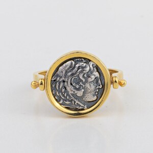 May include: A gold ring with a silver coin featuring a profile of a man's face. The coin is set in a round bezel and the ring has a hinged band.