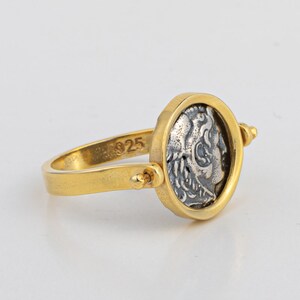 May include: A gold ring with a spinning silver coin featuring a profile of a person's face. The ring is marked with "925" on the band.