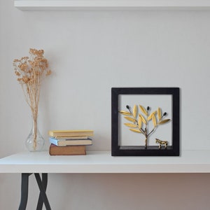 May include: A black framed wall art piece featuring a gold olive branch with black olives and a gold zebra figurine.