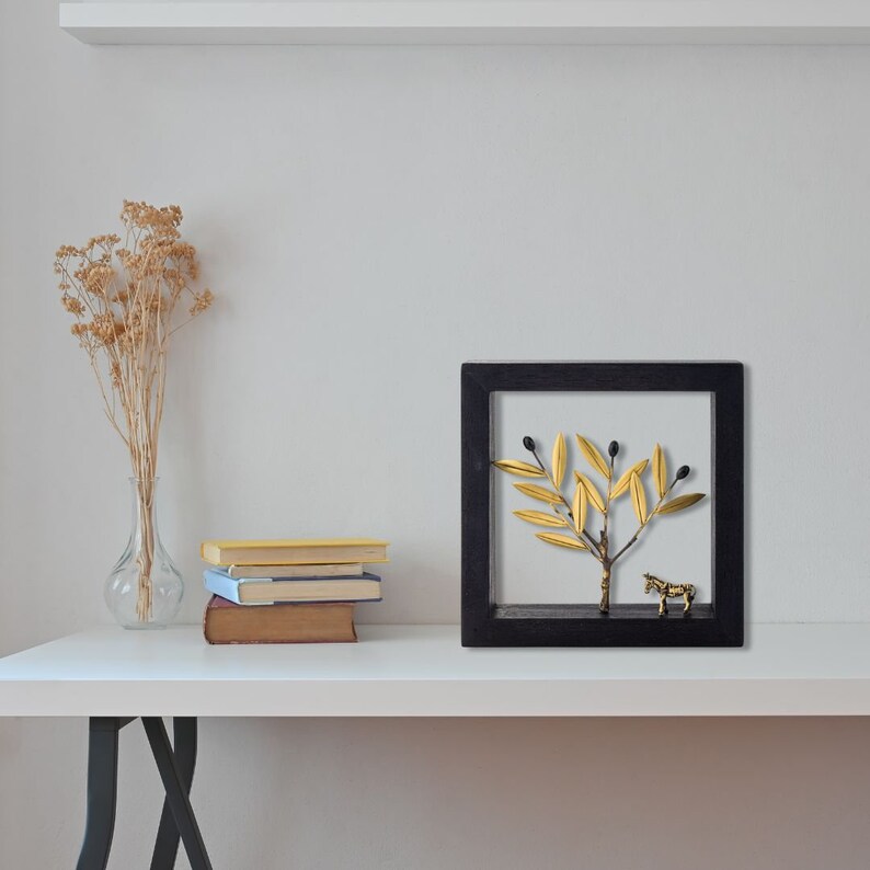 May include: A black framed wall art piece featuring a gold olive branch with black olives and a gold zebra figurine.