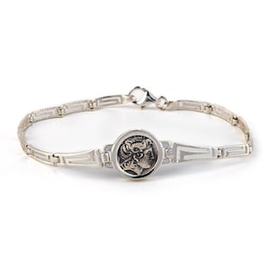 Könnte beinhalten: Ein silbernes Armband mit einem griechischen Münzendesign. Das Armband hat eine silberne Kette mit einem runden Münzenanhänger, der ein Profil einer griechischen Figur zeigt.
