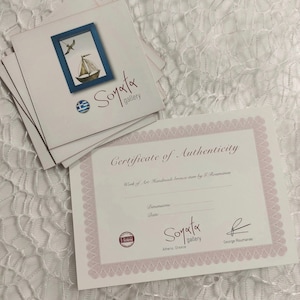May include: Certificate of Authenticity for a handmade bronze item by G. Roumanas. The certificate is printed on white paper with a pink border and features the Soyata Gallery logo and address. The certificate is signed by George Roumanas.