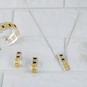Peut inclure: Un ensemble de bijoux en argent et or avec des pierres pr&eacute;cieuses bleues et vertes. L'ensemble comprend un bracelet, un collier et une paire de boucles d'oreilles. Les bijoux pr&eacute;sentent un motif g&eacute;om&eacute;trique.