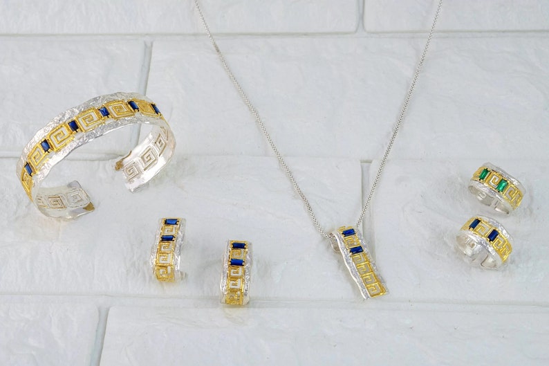 Peut inclure: Un ensemble de bijoux en argent et or avec des pierres pr&eacute;cieuses bleues et vertes. L'ensemble comprend un bracelet, un collier et une paire de boucles d'oreilles. Les bijoux pr&eacute;sentent un motif g&eacute;om&eacute;trique.