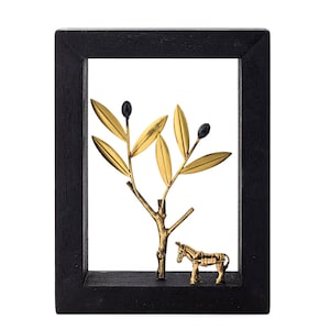 May include: A black framed wall decor with a gold metal olive branch and a donkey figurine. The olive branch has black olives and gold leaves.