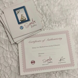 May include: Certificate of Authenticity for a handmade bronze item by G. Roumanas. The certificate is printed on white paper with a pink border and features the text "Soyata gallery" and "Athens, Greece".