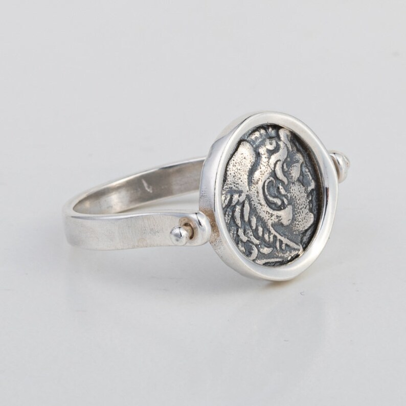 May include: A silver ring with a spinning coin design featuring a detailed profile of a mythical creature. The coin is set in a round bezel and the ring band is plain.