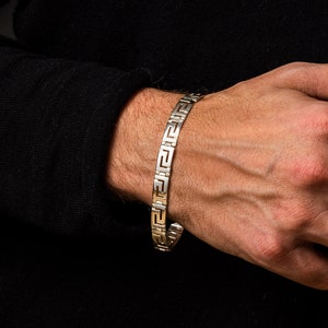 May include: A silver bracelet with a geometric pattern. The bracelet is on a person's wrist.