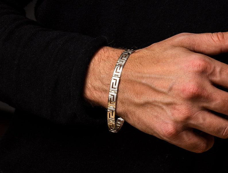 May include: A silver bracelet with a geometric pattern. The bracelet is on a person's wrist.