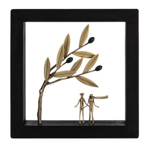 May include: A black framed wall decor with a gold metal olive branch and two gold metal figures standing under the branch. The figures are holding hands.