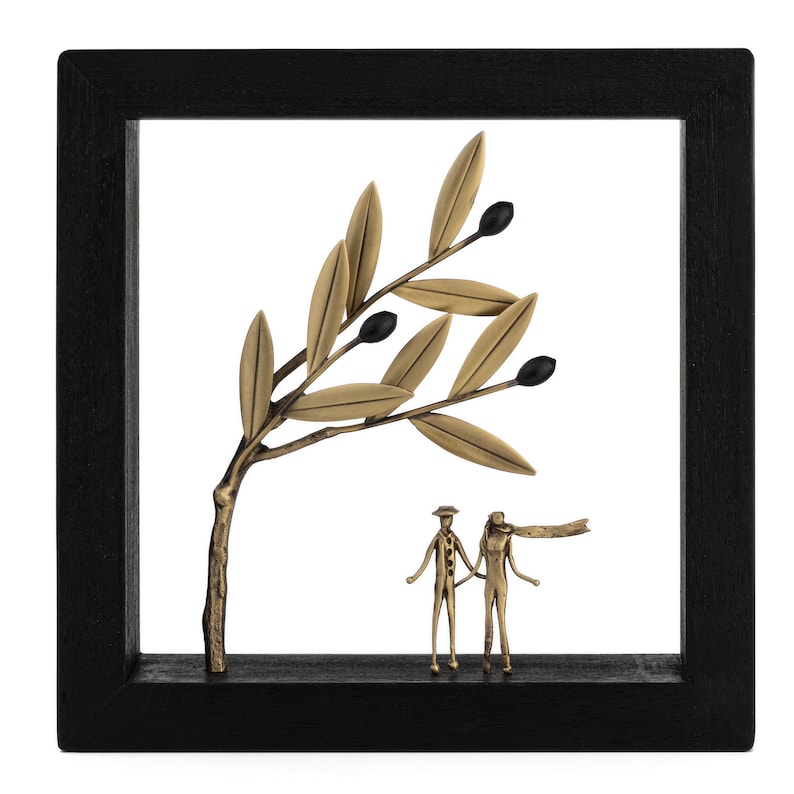 May include: A black framed wall decor with a gold metal olive branch and two gold metal figures standing under the branch. The figures are holding hands.