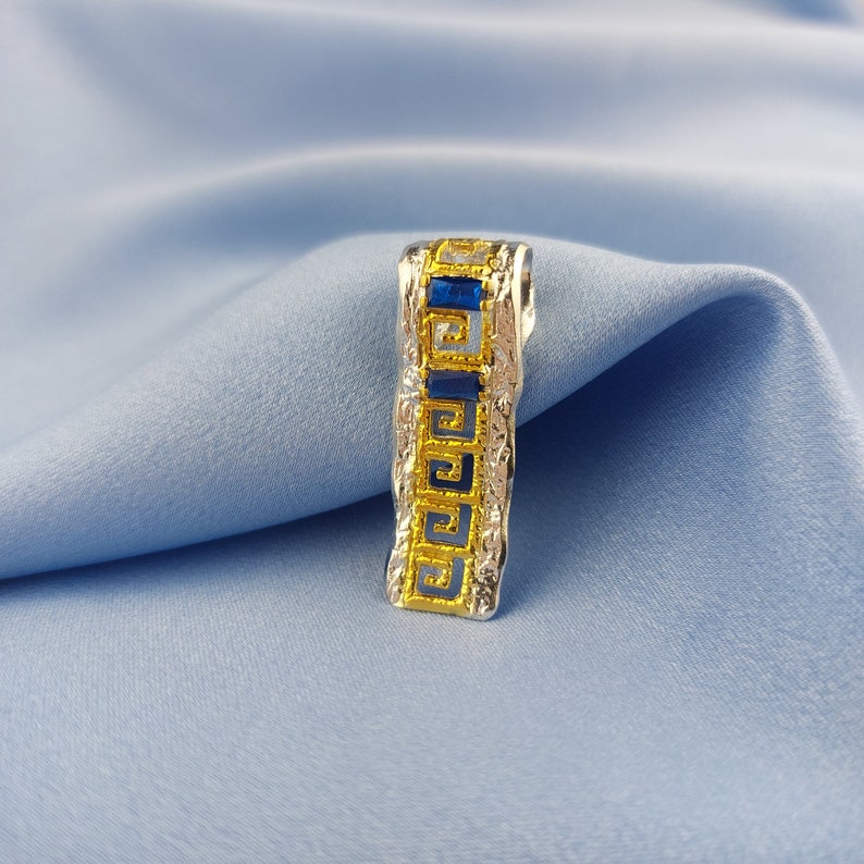 Peut inclure: Un pendentif en argent avec un motif de cl&eacute; grecque dor&eacute;e et des pierres pr&eacute;cieuses bleues.