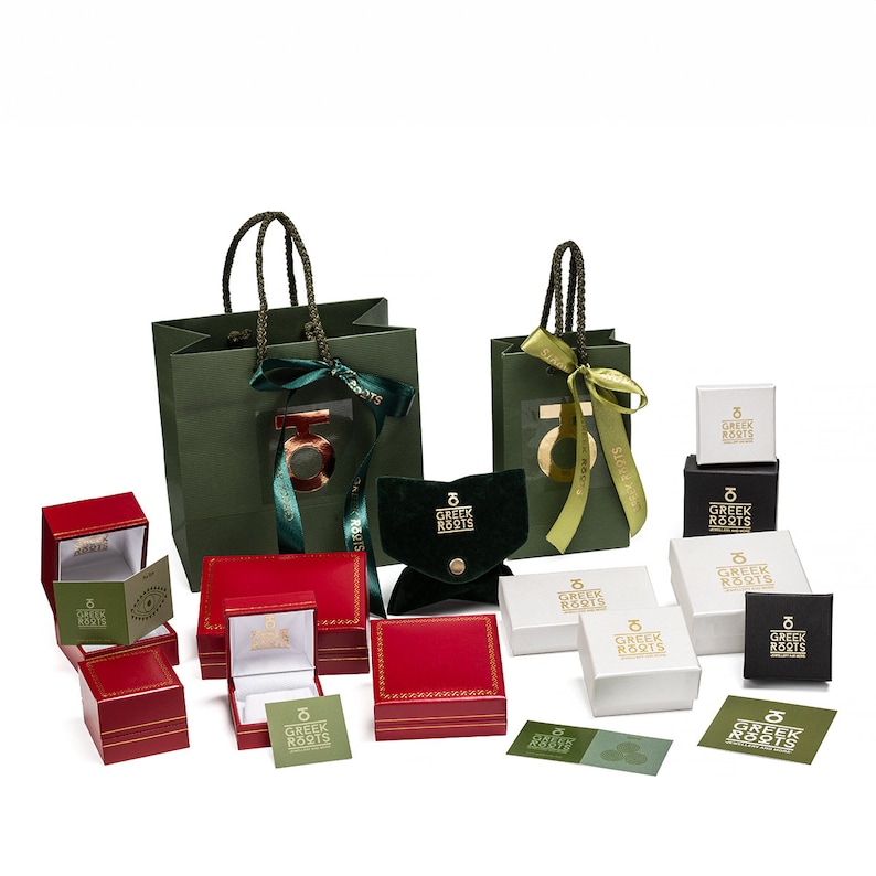 K&ouml;nnte beinhalten: Sortiment von roten und gr&uuml;nen Geschenkboxen mit dem Logo "Greek Roots" in goldenen Lettern. Die Boxen sind auf einer wei&szlig;en Oberfl&auml;che angeordnet.