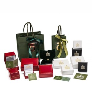 May include: An assortment of red, white and green gift boxes with gold lettering that reads "Greek Roots". The boxes are arranged on a white surface.