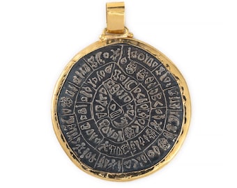 May include: A gold pendant with a black circular disc featuring an intricate design of symbols and letters. The pendant has a textured gold rim.