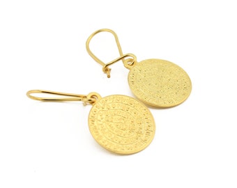 May include: A pair of gold-tone earrings with a circular design featuring intricate details. The earrings are made of metal and have a dangling style.