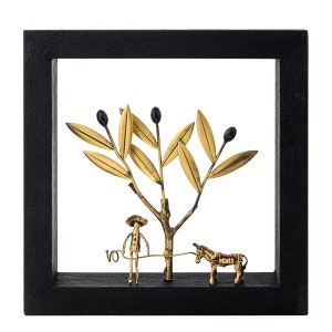 May include: A black framed wall art piece featuring a gold metal olive tree with black olives, a gold metal figure of a person holding a rope, and a gold metal donkey.