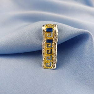 Peut inclure: Un pendentif en argent et or avec un motif de cl&eacute; grecque bleu et or.