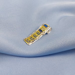 Peut inclure: Pendentif en argent avec un motif de cl&eacute; grecque bleu et or. Le pendentif a une surface textur&eacute;e et une pierre pr&eacute;cieuse bleue.