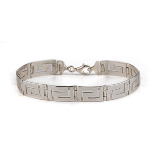 May include: A silver bracelet with a Greek key pattern.