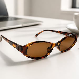 May include: Oval-shaped sunglasses featuring a brown tortoiseshell pattern frame and solid brown tinted lenses. The glasses have a classic curved bridge and thin temples, showcasing a distinct mottled aesthetic with dark and light brown tones.