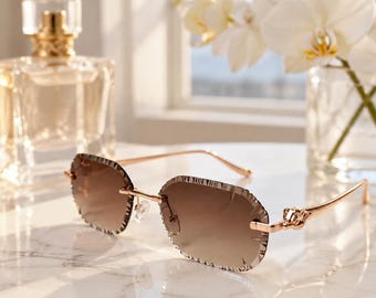 May include: Rimless sunglasses featuring rose gold-tone metal temples and bridge with gradient brown lenses. The lenses have a distinct faceted edge detail around the perimeter, providing a textured look to the frame-less design.