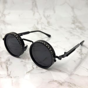 May include: A white ceramic mug with a black handle and the text "But First, Coffee" in a bold, black font. The mug is set against a blurred background, highlighting its clean design.