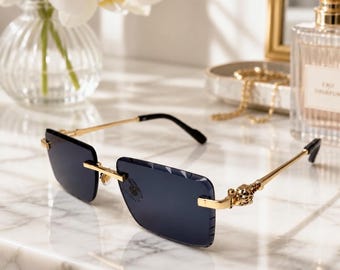 May include: Rimless sunglasses featuring rectangular dark gray lenses and gold-tone metal temples. The hinges are adorned with a detailed gold-tone panther head motif. The bridge and nose pads are constructed from matching gold-tone metal hardware.