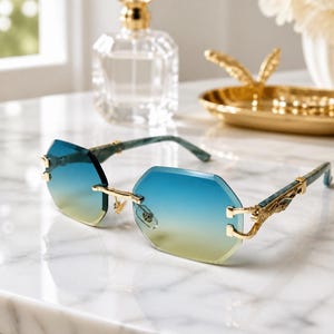May include: Rimless sunglasses featuring octagonal lenses with a blue-to-yellow gradient tint. The frames include gold-tone metal hardware at the bridge and hinges, connected to patterned teal and white marbled temples with intricate gold-tone detailing.