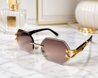 May include: Rimless sunglasses featuring octagonal brown gradient lenses. The frames include gold-tone metal accents at the hinges and bridge, with black temples adorned with a detailed gold-colored dragon motif on the side near the lens connection.