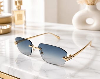 May include: Rimless sunglasses featuring rectangular gradient blue lenses that transition to clear. The gold-tone metal temples are accented with a detailed leopard head design at the hinges, connecting to a thin gold bridge and nose pads.