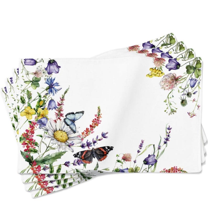 K&ouml;nnte beinhalten: Set mit vier wei&szlig;en Leinen-Platzsets mit einem Aquarell-Blumendesign. Die Platzsets zeigen eine Vielzahl von Blumen, darunter G&auml;nsebl&uuml;mchen, Lavendel und Glockenblumen, sowie Schmetterlinge in Blau- und Rott&ouml;nen.