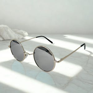 May include: Round sunglasses with silver frames and dark gray lenses. The sunglasses have a classic design with a thin metal frame and black temple tips. The lenses are circular and reflect the light.