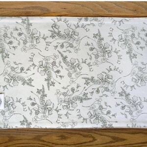 K&ouml;nnte beinhalten: Ein wei&szlig;er Platzdeckchen aus Baumwolle mit einem schwarzen Blumenmuster. Das Muster zeigt zarte Blumen und Bl&auml;tter.