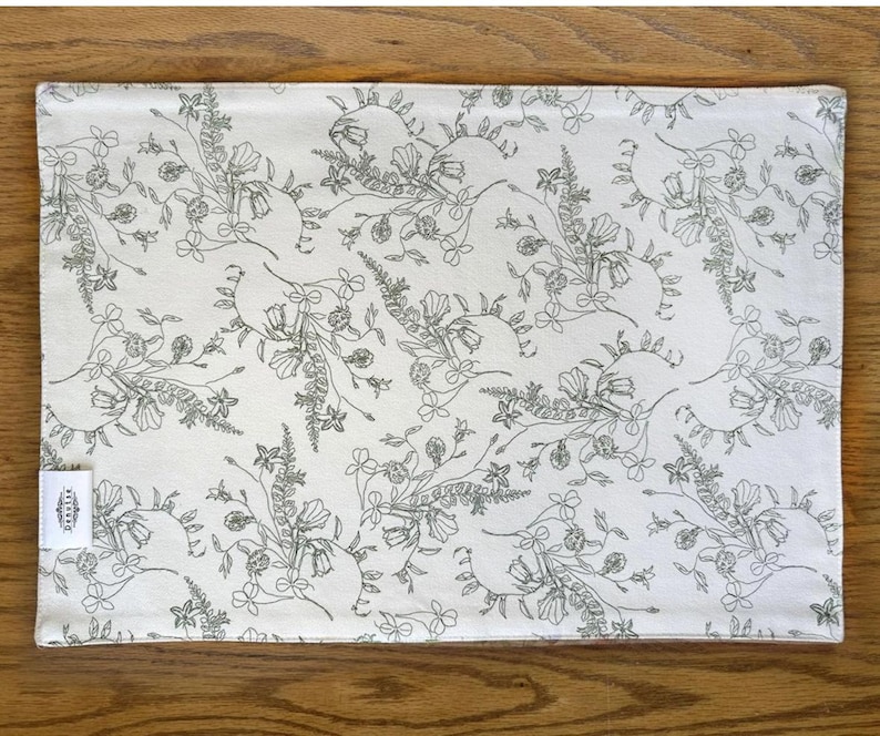 K&ouml;nnte beinhalten: Ein wei&szlig;er Platzdeckchen aus Baumwolle mit einem schwarzen Blumenmuster. Das Muster zeigt zarte Blumen und Bl&auml;tter.