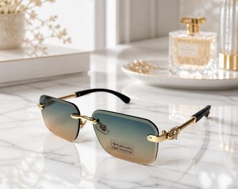 May include: Rimless sunglasses featuring a gold-tone metal frame with twisted temple arms and black tips. The rectangular lenses display a gradient transition from blue at the top to amber at the bottom, with a sticker reading Photochromic UV400 PROTECTION.