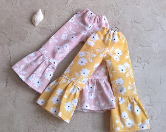 May include: Two pairs of baby trousers with a floral pattern. One pair is pink, and the other is yellow. Both have white flowers and a flared leg design. The trousers are made of a soft fabric and are suitable for infants.