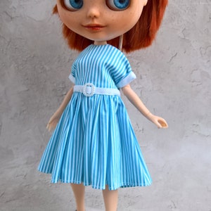 May include: A blue and white striped dress with a white belt and a white buckle. The dress is pleated and has a fitted bodice.